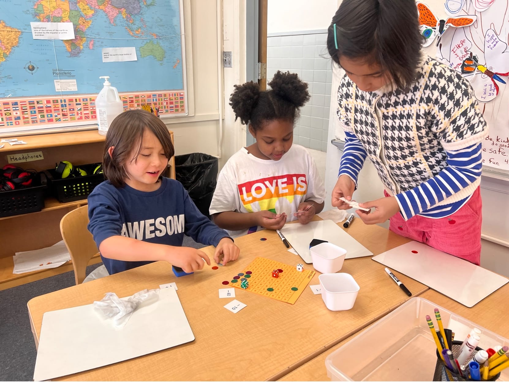 Three Lower School students play a place value dice game at their classroom table