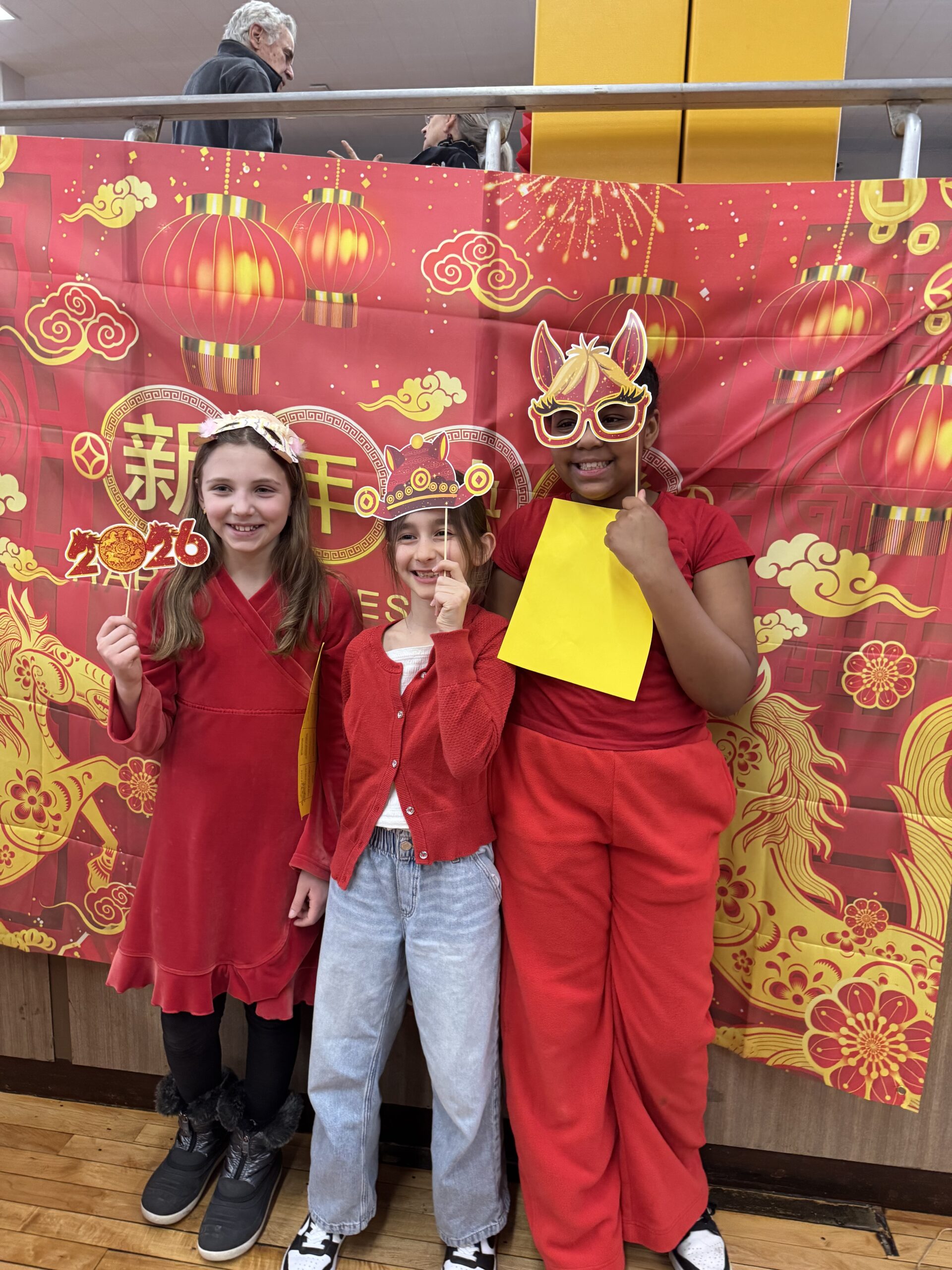 Three students dressed in red hold festive props at the Hudson School Lunar New Year celebration