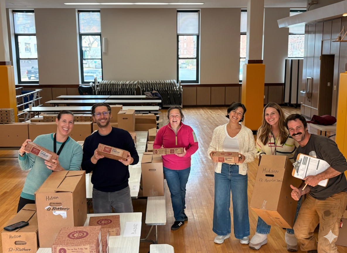 Parent volunteers hold fundraiser pie boxes among packed cartons in the school cafeteria