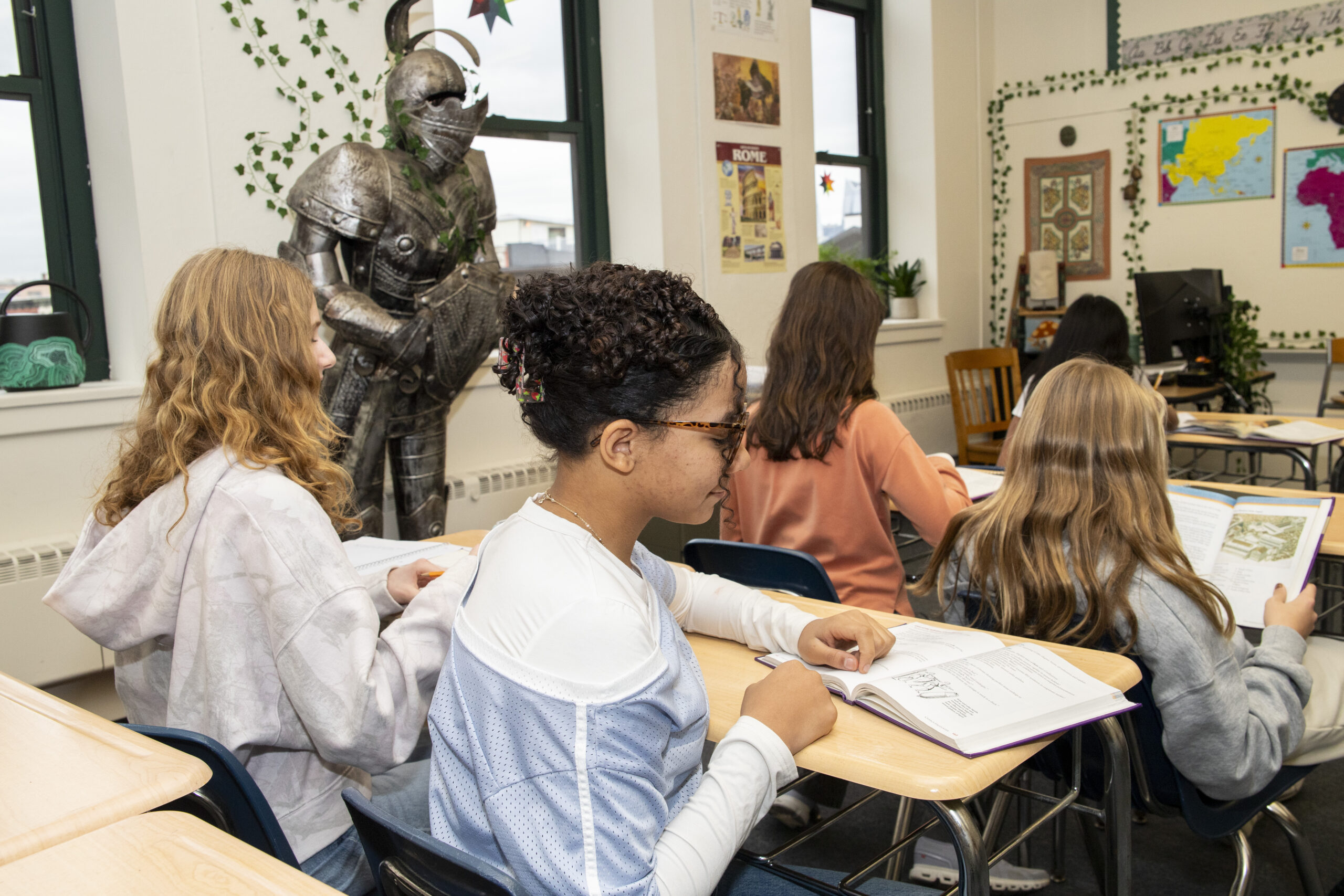 Students read history textbooks at their desks beside the classroom suit of armor