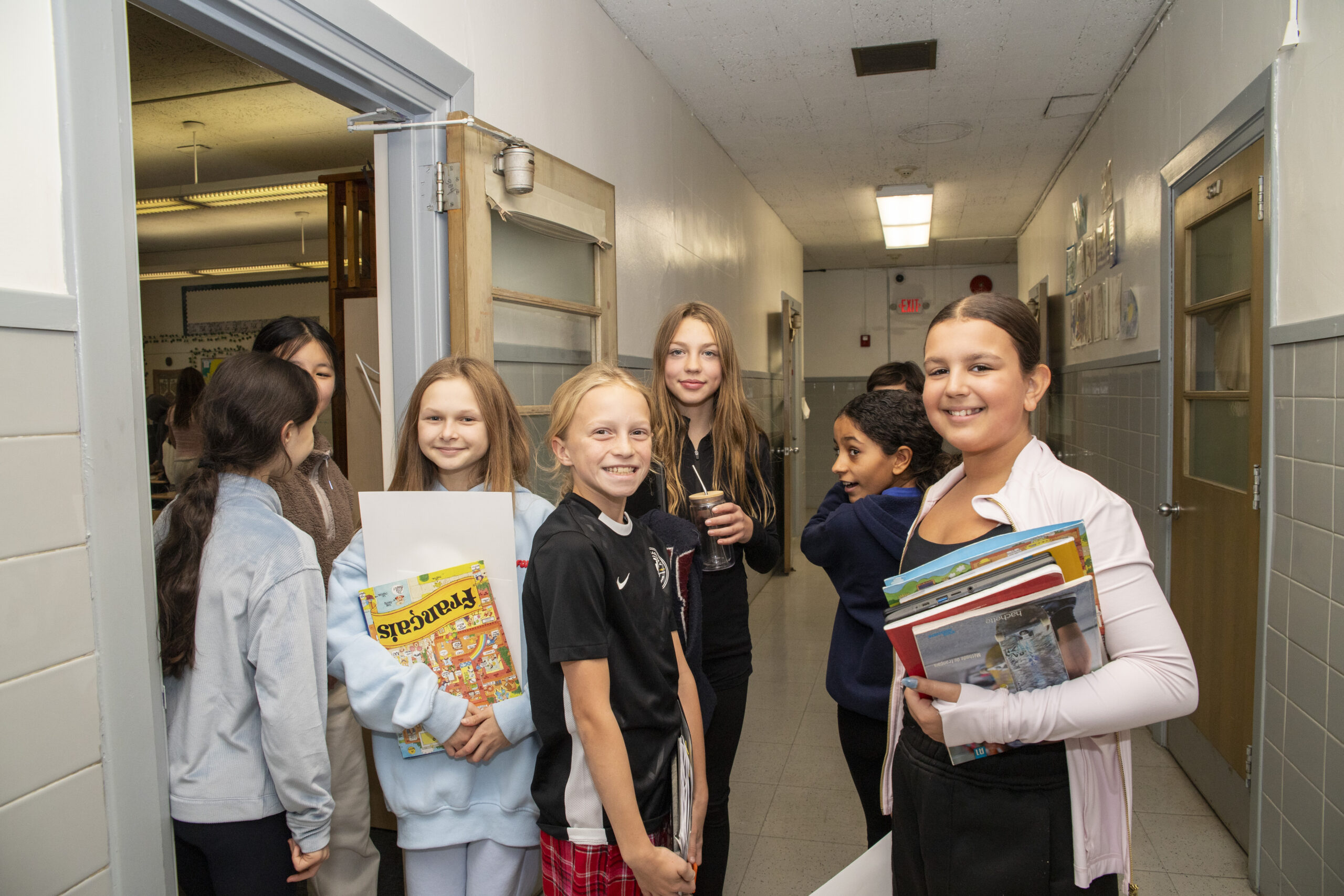 Middle school students carrying books and a French workbook chat in the hallway