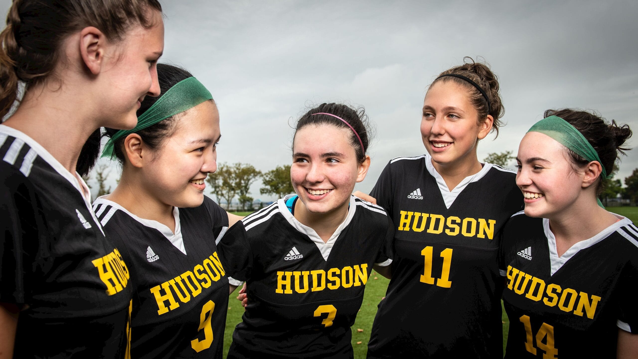 Hudson girls soccer players huddle and smile together before a game