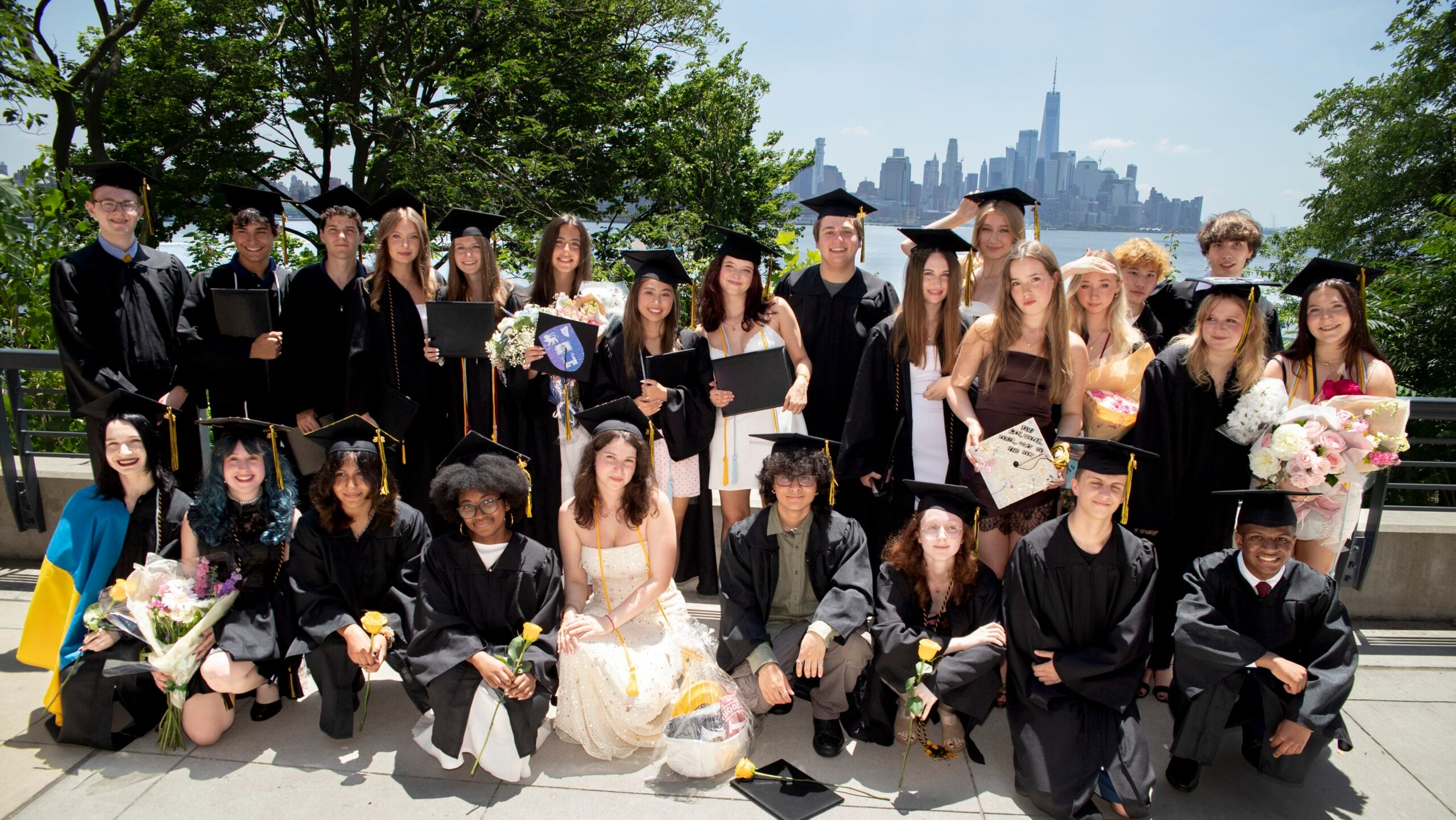 Graduates in caps and gowns pose with the Manhattan skyline across the Hudson River